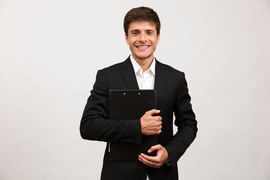 Businessman standing isolated holding clipboard looking camera.