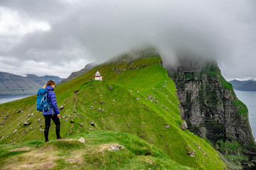 Unrecognizable female hiker stands on top of hill and looks towards lighthouse.