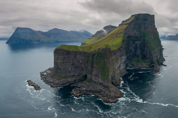 AERIAL: Flying around a grassy islet with black rocky cliffs towering over sea.
