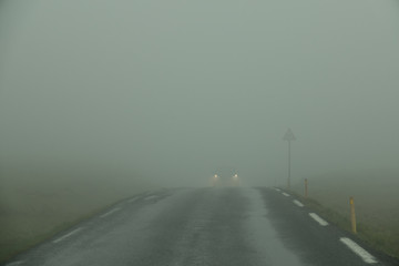 Car drives through the thick white fog down an empty country road in Scandinavia