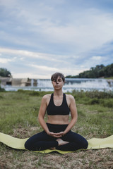 Fototapeta na wymiar Young beautiful woman doing yoga exercises in park on the bank river in the summer