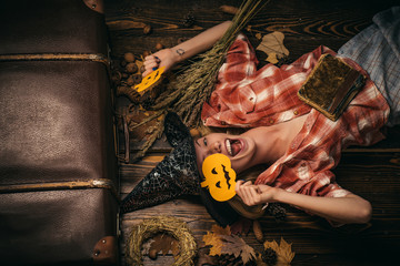 Cheerful girl play with pumpkins. Funny woman in carnival costumes on wood background. Smiling girl...
