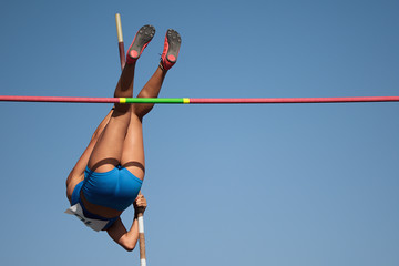 Competition pole vault jumper female on blue sky background - obrazy, fototapety, plakaty