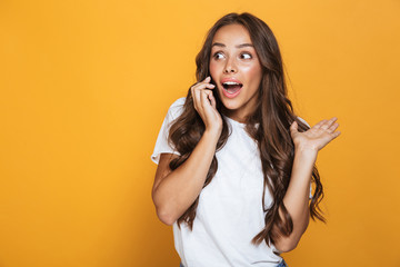 Portrait of european woman 20s with long hair shouting and talking on mobile phone, isolated over yellow background