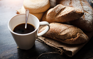 The blurry light design background of ceramic coffee cup put beside group baguette and bun,on wooden desk,vintage tone