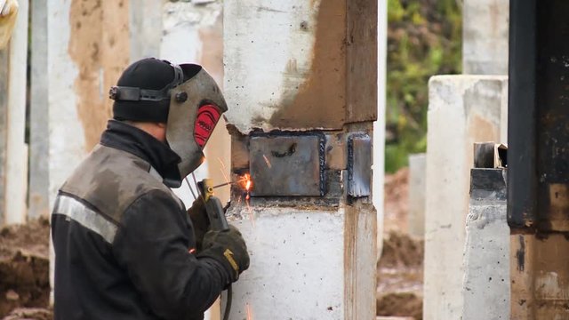 Construction of the road. A worker in a special mask solder a metal part to the base of the bridge to build a new road