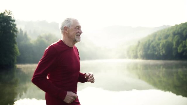 Senior man running by the lake outdoor in foggy morning in nature.