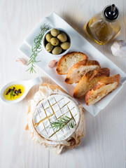 Baked camembert cheese. Fresh Brie cheese and a slice on a wooden board with nuts, honey, rosemary, baguette bread grilled toasts and leaves. Brie type of cheese. Italian, French cheese.