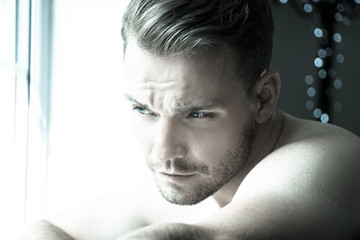 Hunky muscular, sexy shirtless man with defined abs and muscles looks out of window