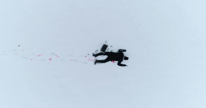 Aerial footage. Dead man on snow with gun and case of cash. Camera moves up. 4K video
