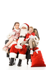 Obraz premium happy kids and santaembracing and looking at camera while sitting in armchair together isolated on white