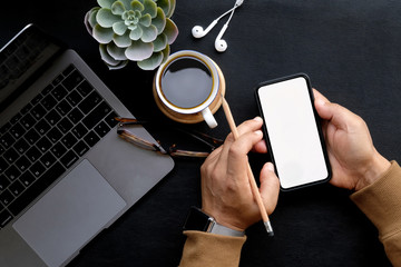 Man using mobile smartphone on dark home business desk.