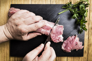 man's hands splitting a pork tenderloin with a knife next to some parsley branches on a black slate griddle on a wooden table
