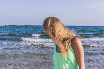 A woman with her hair loose in the wind is out of focus on the background of the sea