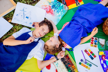 Authentic artist children in blue aprons girl and boy paints tickle each other by paint brushes,...