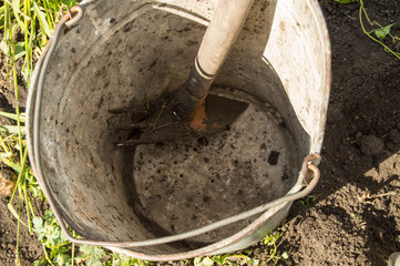 Close-up of an old dirty rusty iron bucket with rake on the background of soil and grass in the...