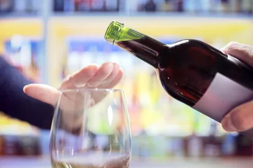 Gardinen Frauenhand, die mehr Alkohol aus der Weinflasche in der Bar ablehnt © Brian Jackson