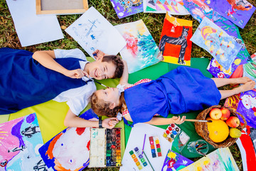 Authentic artist children in blue aprons girl and boy paints tickle each other by paint brushes,...