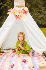 Little girl lying and playing in a tent, children's house wigwam in park Autumn portrait of cute curly girl. Harvest or Thanksgiving. autumn decor, party, picnic. Child in halloween costume. © MartaKlos