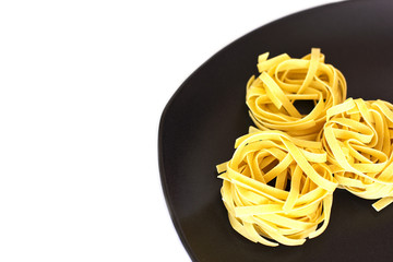 Uncooked tagliatelle on a ceramic plate. Isolated
