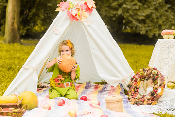 Little girl lying and playing in a tent, children's house wigwam in park Autumn portrait of cute curly girl. Harvest or Thanksgiving. autumn decor, party, picnic. Child in halloween costume. © MartaKlos