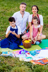 Rear view of parents with two children son and daughter paitners in aprons hugging together sitting on grass, picnic time over their house on background. The concept of a happy family.