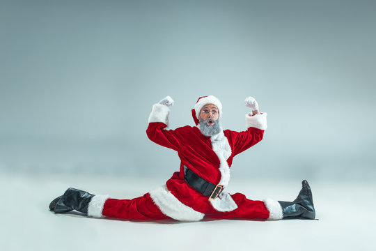 Funny serious guy with christmas hat dancing at studio. New Year Holiday. Christmas, x-mas, winter, gifts concept. Man wearing Santa Claus costume on gray. Copy space. Winter sales.