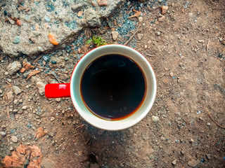 Red and white cup with dark coffee on the ground