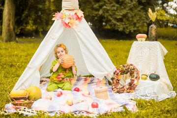 Fototapeta na wymiar Little girl lying and playing in a tent, children's house wigwam in park Autumn portrait of cute curly girl. Harvest or Thanksgiving. autumn decor, party, picnic. Child in halloween costume.