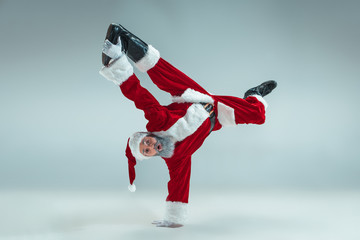 Funny serious guy with christmas hat dancing at studio. New Year Holiday. Christmas, x-mas, winter, gifts concept. Man wearing Santa Claus costume on gray. Copy space. Winter sales.