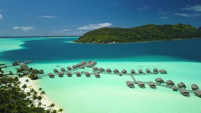Aerial footage from a drone of luxury overwater villas with palm trees, blue lagoon, white sandy beach and Otemanu mountain at Bora Bora island, Tahiti, French Polynesia (Bora Bora Aerial)
