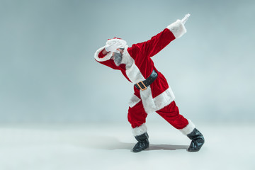 Funny serious guy with christmas hat dancing at studio. New Year Holiday. Christmas, x-mas, winter, gifts concept. Man wearing Santa Claus costume on gray. Copy space. Winter sales.