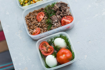 Diet food in the three containers on a gray background. Boiled and fresh vegetables, buckwheat, eggs, beef, chicken.