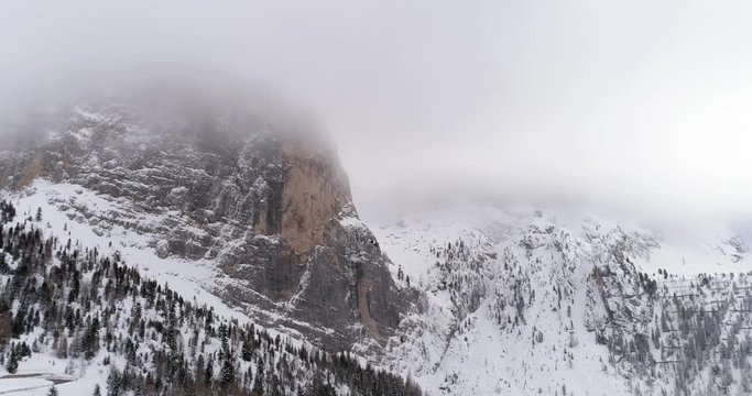 Backward aerial with snowy mountain and woods forest at Sella pass.Cloudy bad overcast foggy weather.Winter Dolomites Italian Alps mountains outdoor nature establisher.4k drone flight