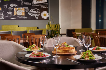 Cozy family restaurant, cafeteria, cafe, bar. The festive table is served with an abundance of dishes and awaits guests, customers, visitors, a big company. Five gourmet dishes and pizza in the center