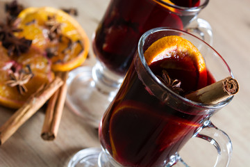 Mulled wine in glass with spice and fruit on wooden table.