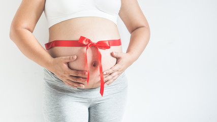 Close up image of pregnant woman tummy with red ribbon.