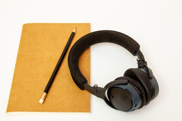 Photograph of a blank brown note book and wireless headphones. isolated on white background.