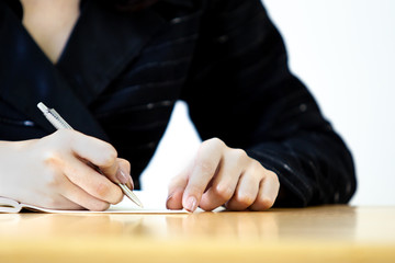 Business women in black suit writing in a notebook close up on her hands.