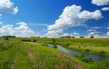 Sunny summer landscape with river,fields,green hills,hay bales and beautiful clouds in blue sky.River Upa in Tula region,Russia. 