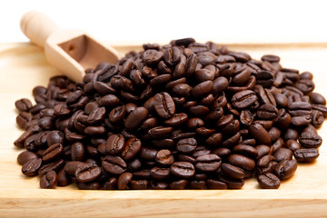 Medium roasted organic coffee beans on wooden plate close up.