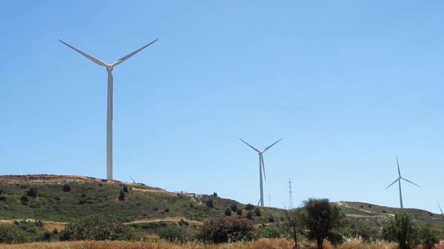 Green hill with windmills in Larnaca, Cyprus. Wind power technology - wind turbine against blue sky spinning in slow motion. Clean and renewable energy resource of alternative energy production
