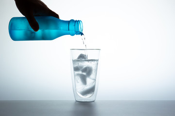 Man filling water from the blue plastic bottle into double glass.  Lighting set up shot on white background.  Concept of good health and refreshment.