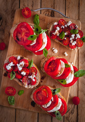 Bruschetta with cheese, tomatoes, fresh basil and balsamic vinegar on cutting board, top view