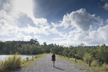 Young woman walking the forest road with beautiful view on the lake in the Khao Yai National park with blue and cloudy sky.