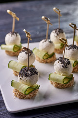 An unusual beautiful appetizing appetizer for a festive table. Mini canapes from a piece of baguette with sesame, thin slice of cucumber and a ball of cheese. Exotic black sesame for decoration.
