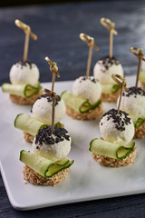 An unusual beautiful appetizing appetizer for a festive table. Mini canapes from a piece of baguette with sesame, thin slice of cucumber and a ball of cheese. Exotic black sesame for decoration.