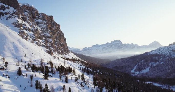 Forward aerial to snowy valley with woods forest at falzarego pass.Sunset or sunrise, clear sky.Winter Dolomites Italian Alps mountains outdoor nature establisher.4k drone flight