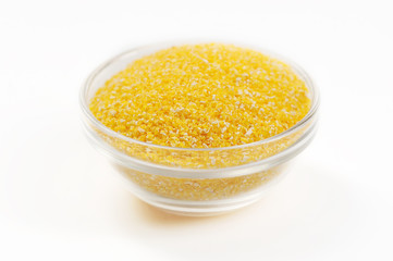 Corn meal in a glass bowl. White background. Close-up. Macro photography.