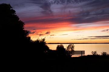Fototapeta premium Sunset silhouette with bench and shoreline